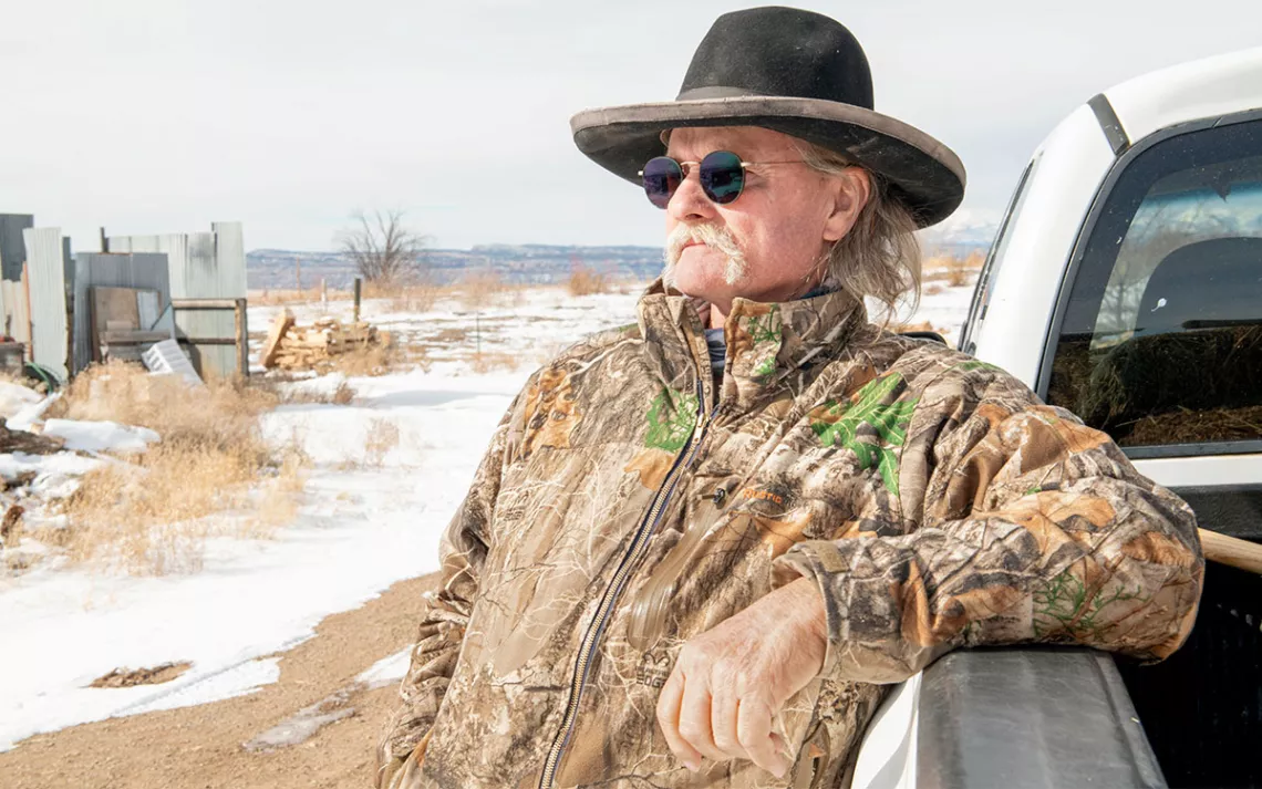Roger Carver wears a hat, sunglasses, and camo jacket and leans on a truck