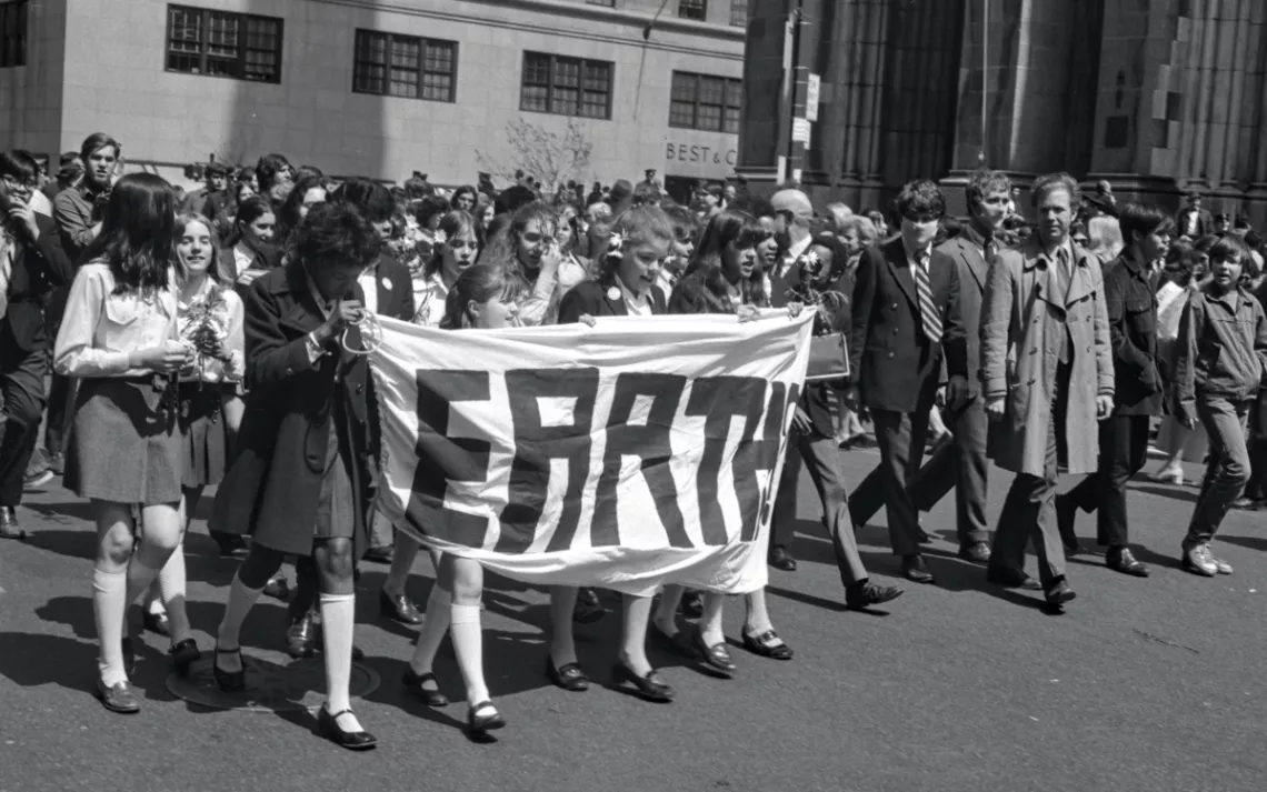 Students in their school uniforms walk and hold a banner that says Earth, on the first Earth Day in 1970.