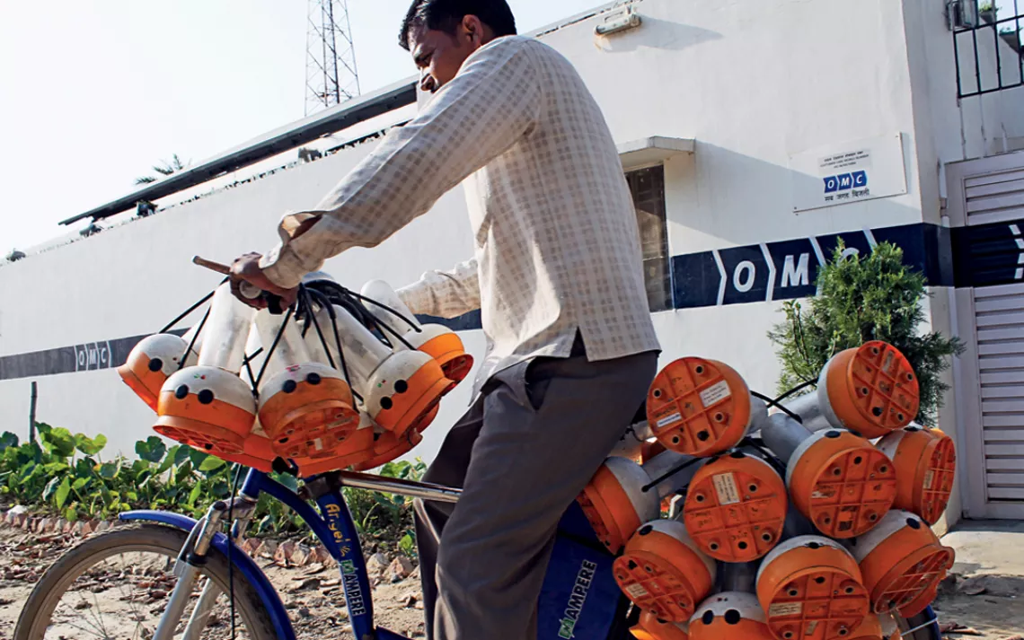 A deliveryman leaves OMC's Jangaon plant on a bike loaded with fully charged lanterns. In the background, a telecom tower operates  on solar energy provided by the same plant.