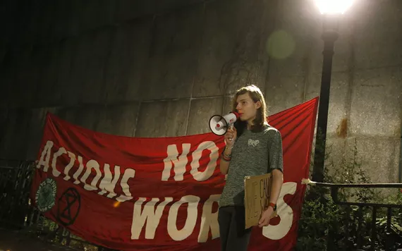 Young woman speaking into a megaphone in front of a red banner that reads "Actions, not Words."