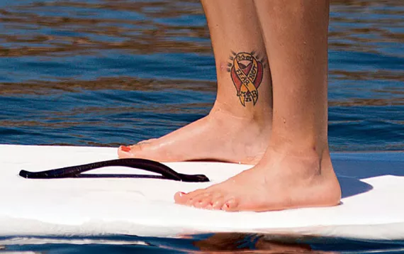 Knees bent, feet shoulder-width apart, Margaux Vair coasts on a standup paddleboard. Vair's tattoo commemorates her fallen comrades—Sergeants Michael Peek, Ashly Lynn Moyer, and Brandon Parr—who died in Iraq on March 3, 2007.
