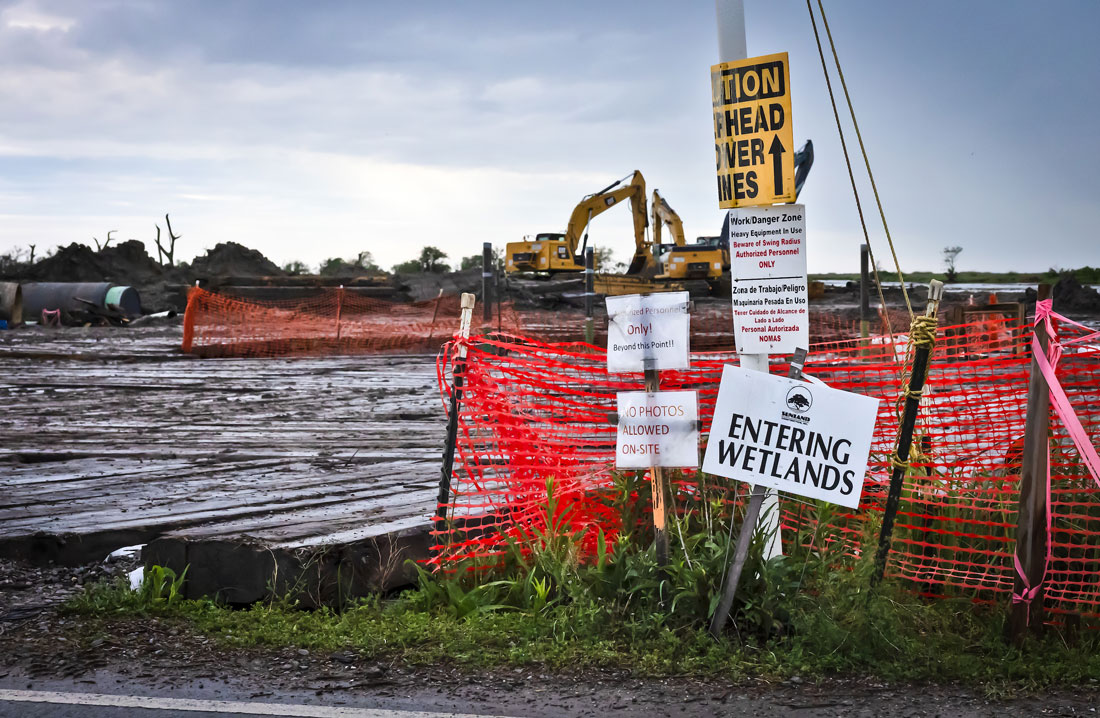 Scene at a construction site with netting and “Entering Wetlands” sign in foreground