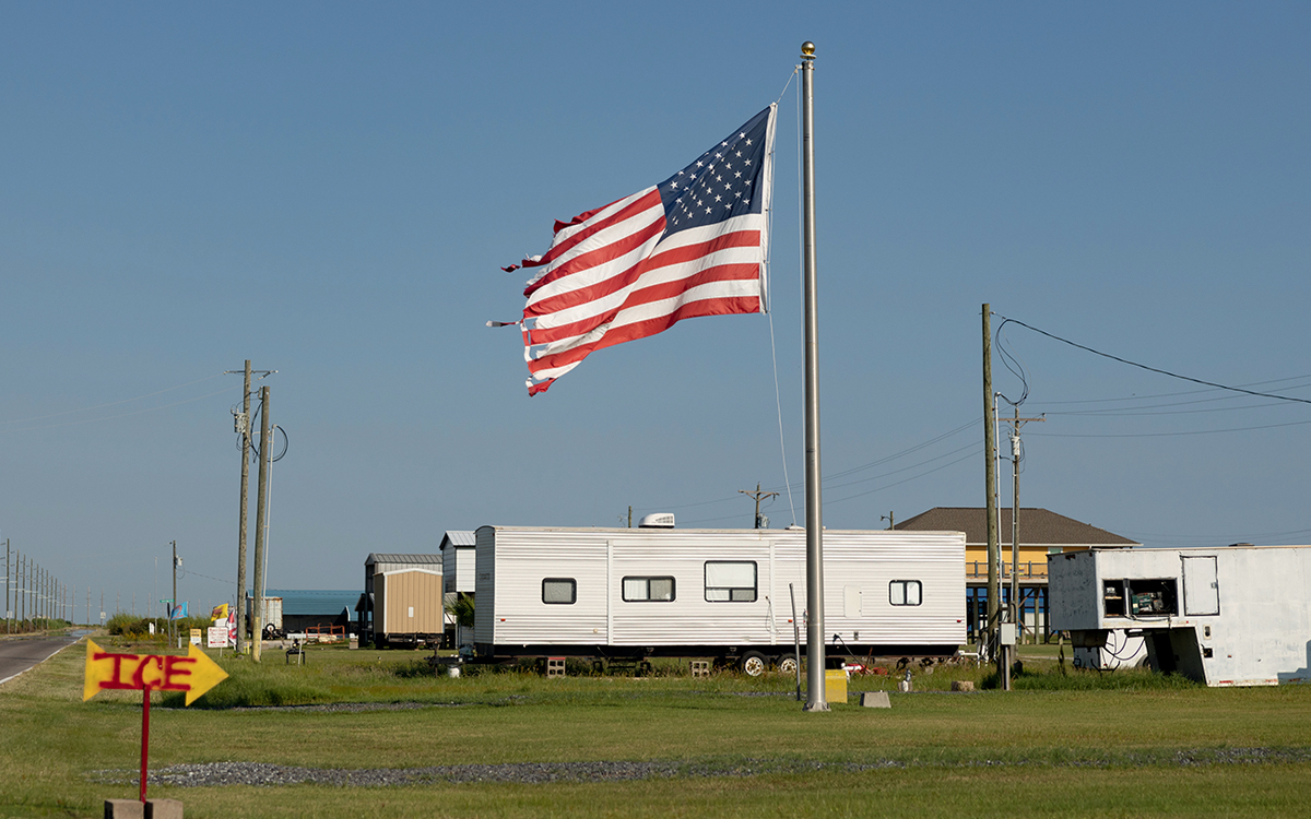 A tattered flag waves in front of temporary housing.