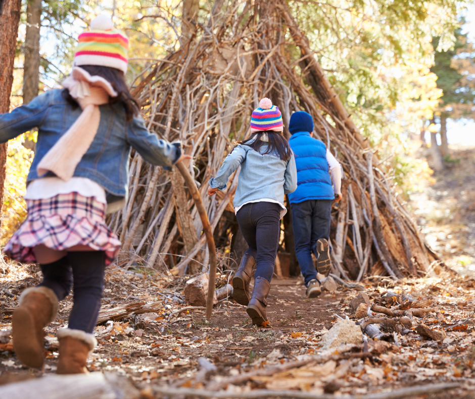 Three young children playing in the woods near a handmade wood structure
