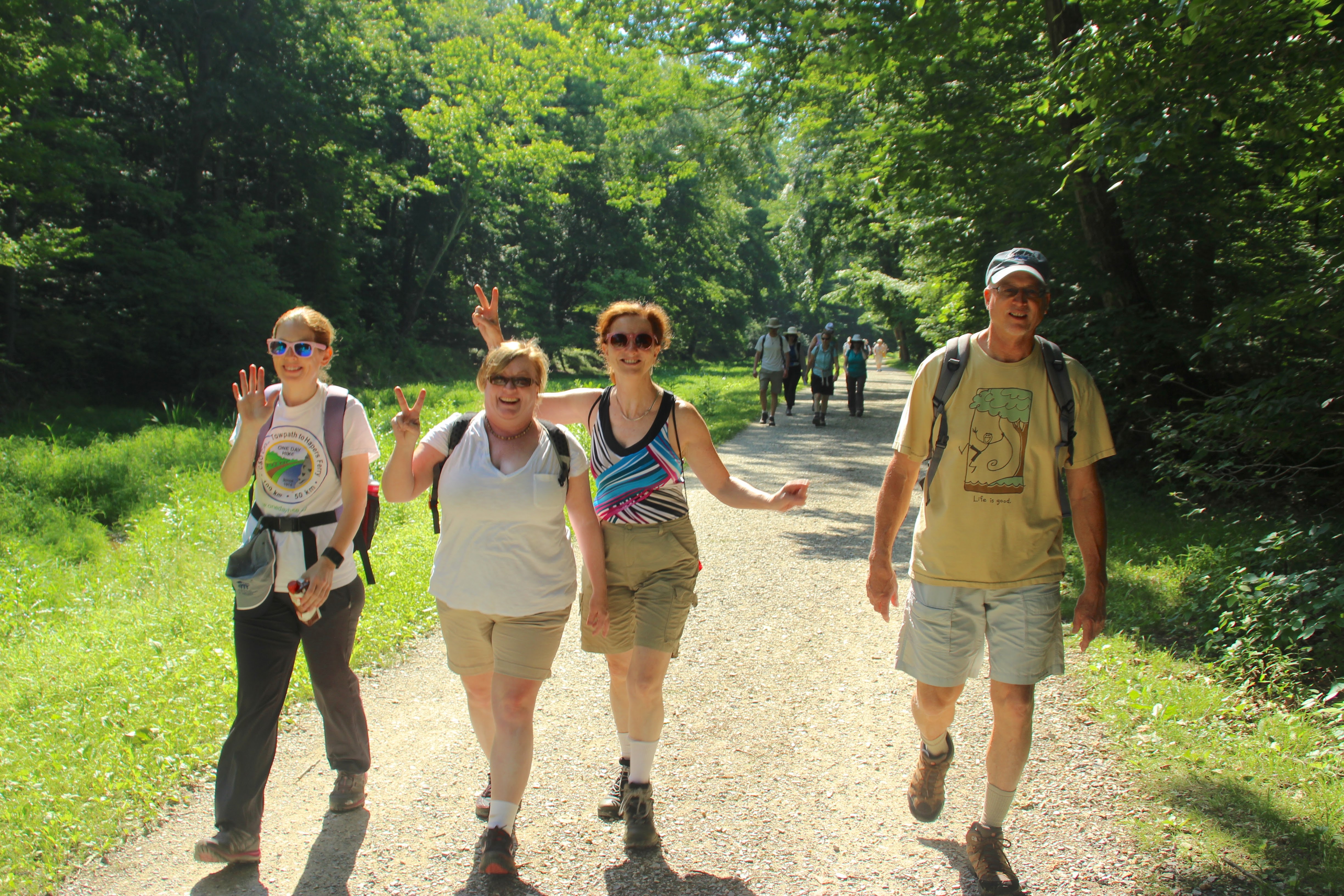 A group of people smile and put up peace signs as the walk on the trail
