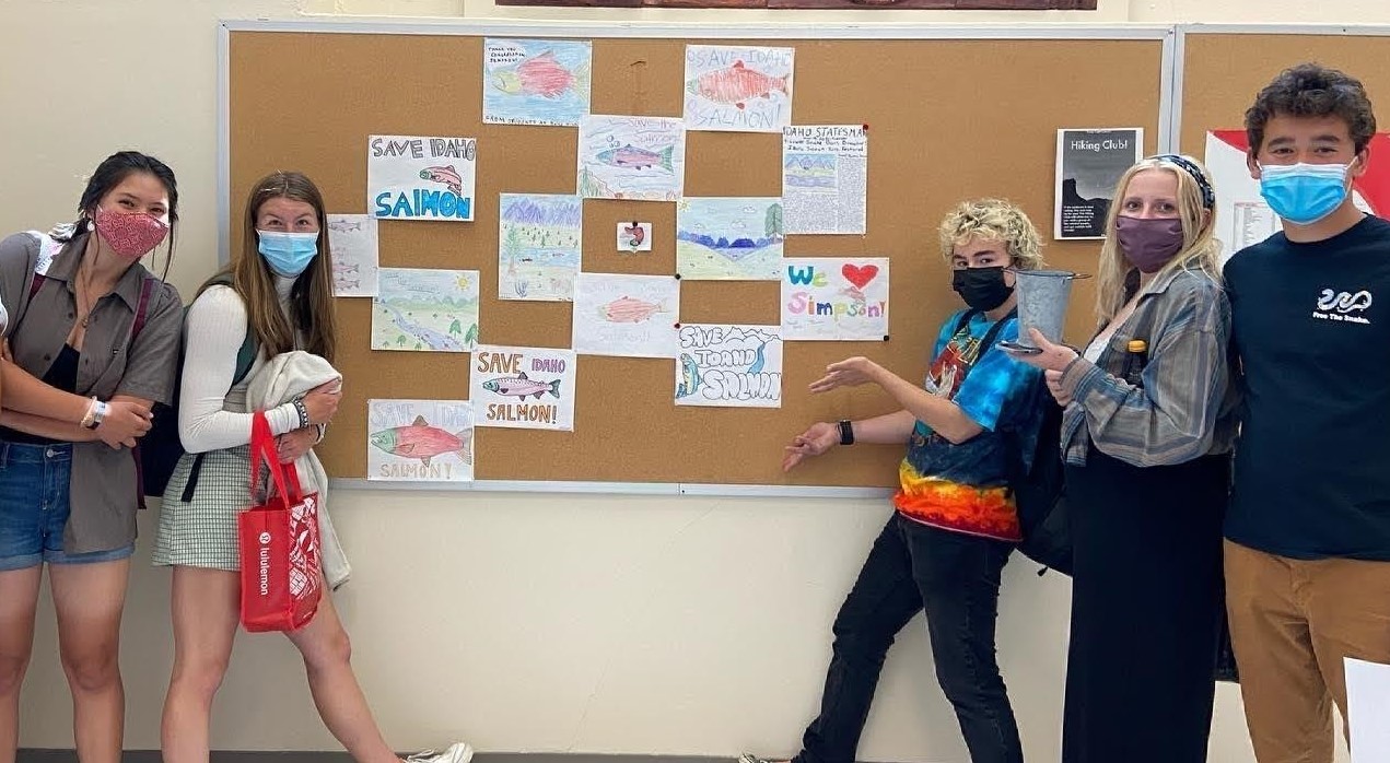 High school students standing by a bulletin board that has hand-drawn pictures that say "Save Idaho Salmon"