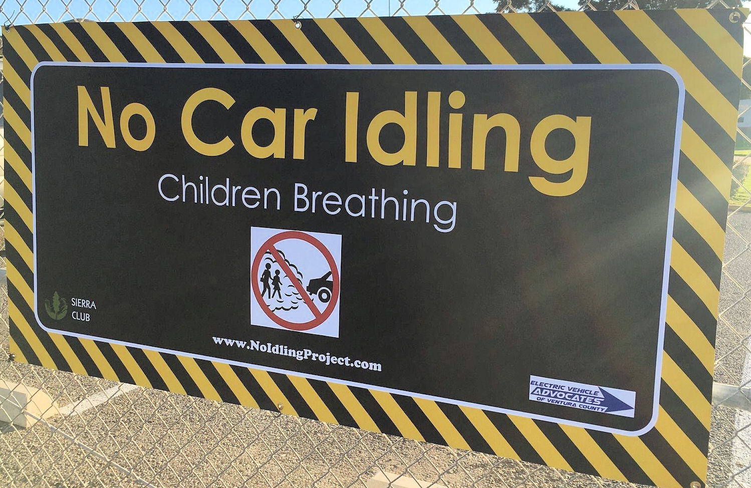 A sign in yellow and black reads "No Car Idling, Children breathing"