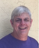 Jim Teas, a caucasian man with white hair, smiling in a purple shirt