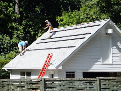 Two men building something on a peaked roof, the same roof as the one with the solar panels in the other photo