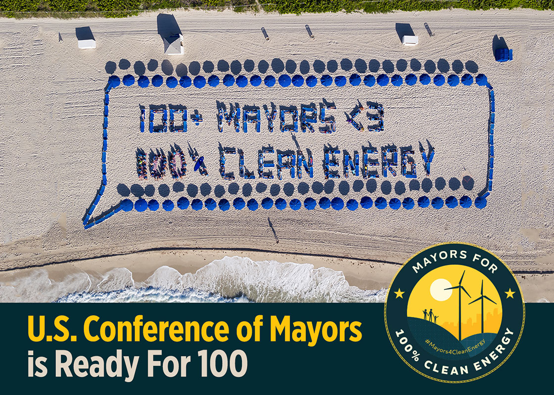 Aerial shot of the phrase "100+ Mayors <3 Clean Energy" spelled out by RF100 leaders on a beach