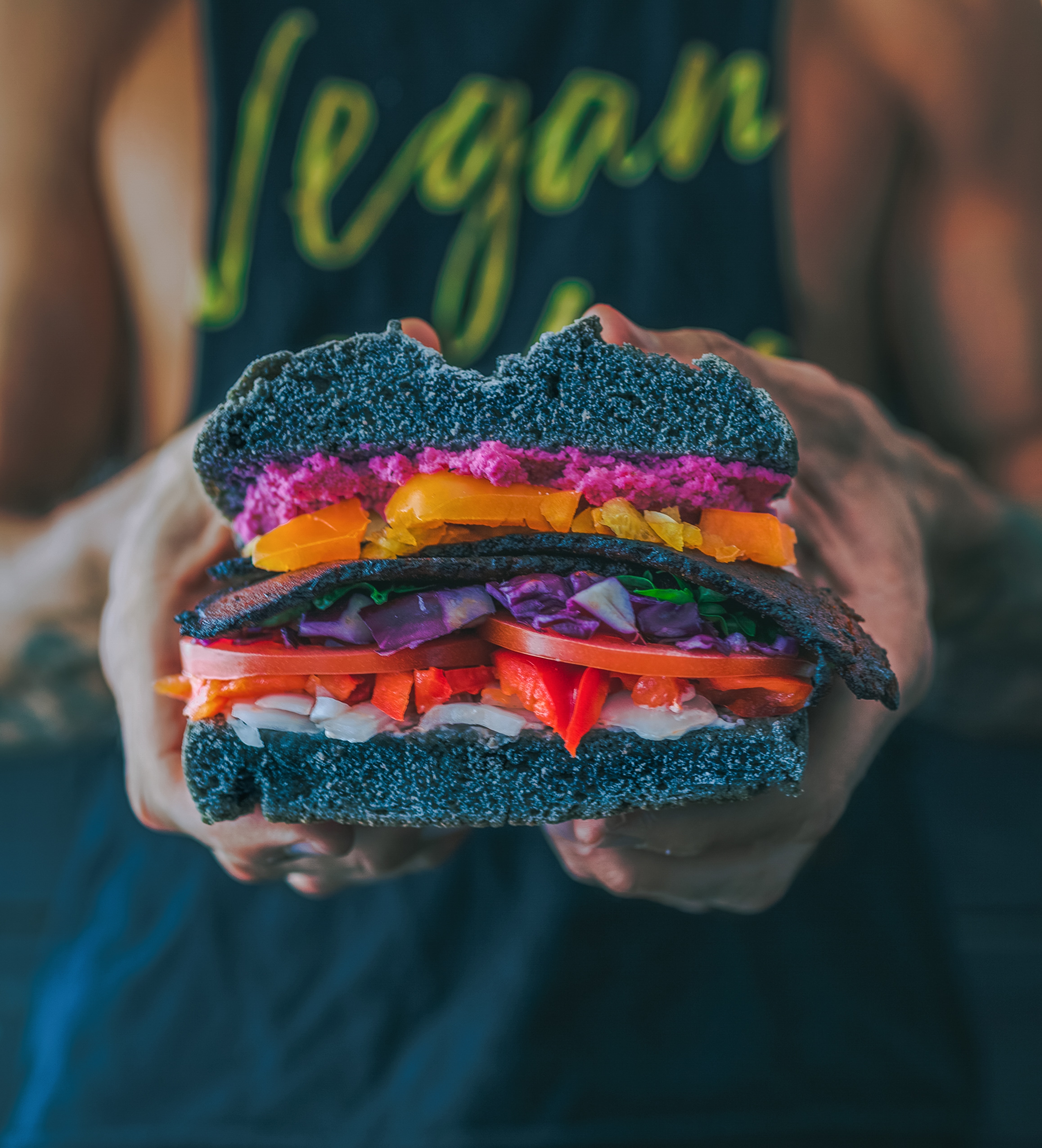 Man in black top that says vegan holding a veggie sandwich with black buns