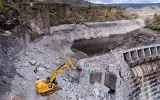 Aerial photo of the dismantling of Copco 1 Dam shows the water line of the former reservoir, an excavator, and workers.