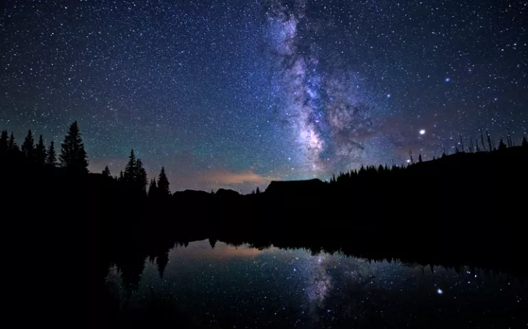 A purple nighttime sky full of stars and its reflection in a lake