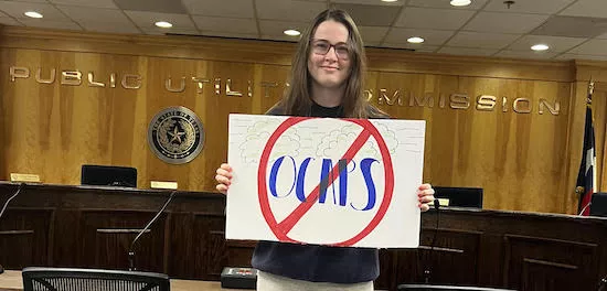 Woman stands in agency meeting room with sign that says No to OCAPS