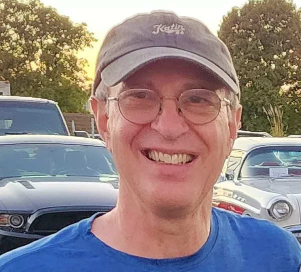 A man with a grey baseball cap and glasses smiling for the camera.