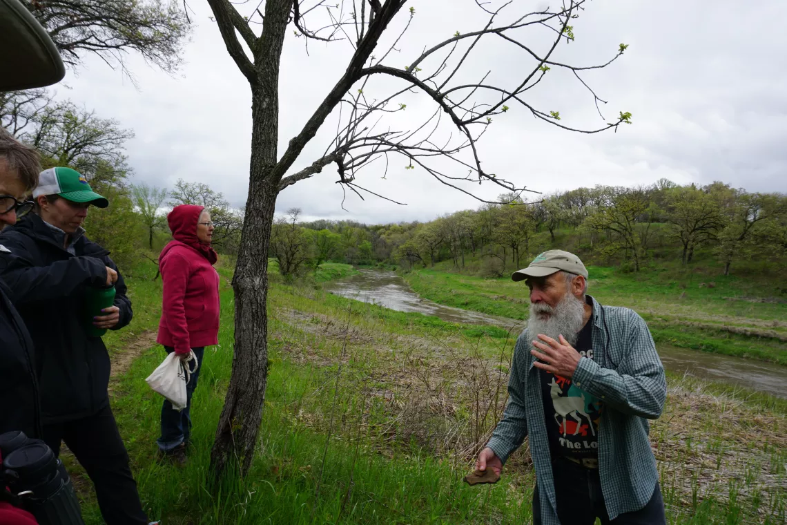 Dr. Tom Rosburg stands in front of a seep and the Raccoon River at Whiterock Conservancy, Coon Rapids, IA