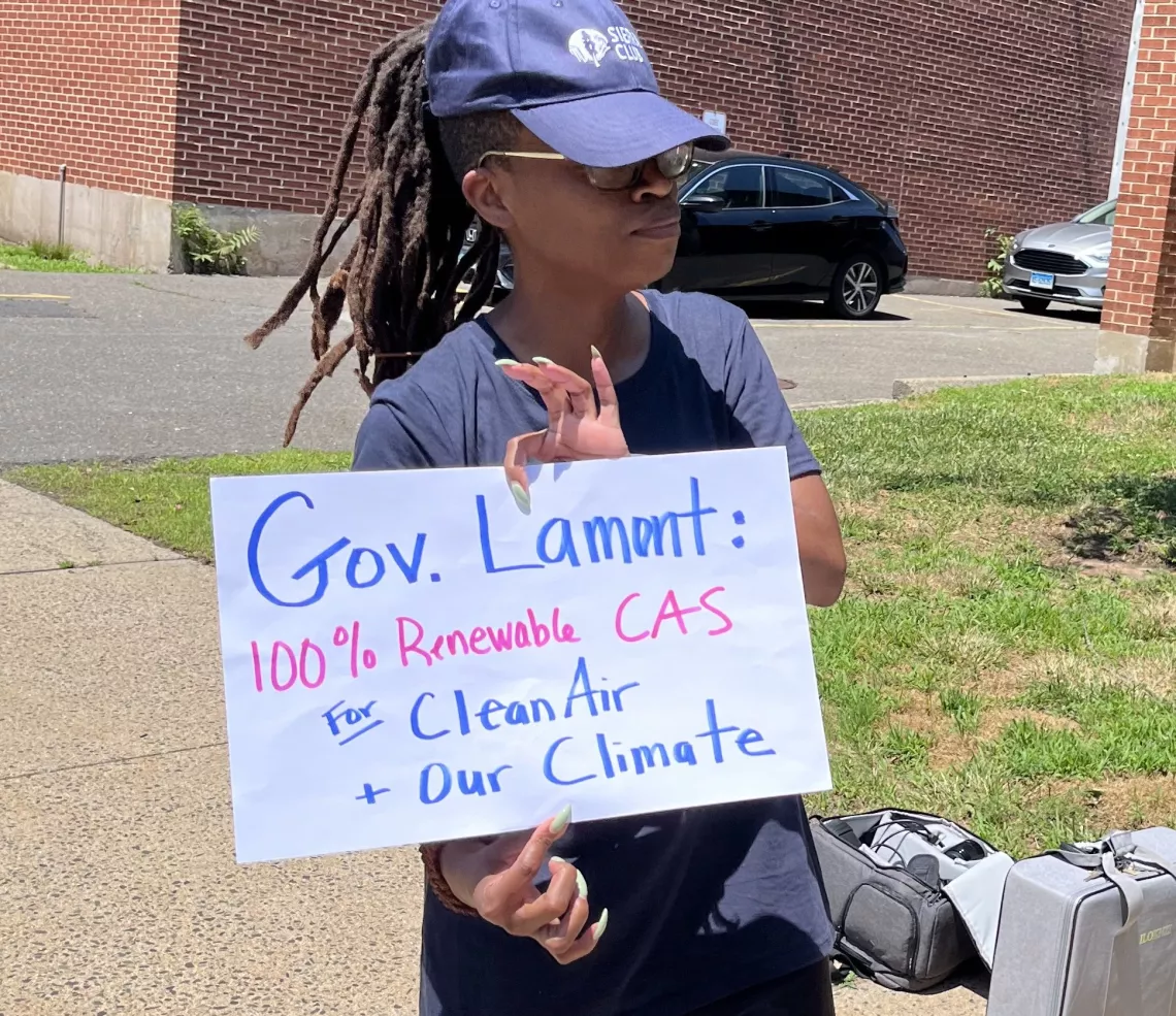 Woman holds sign reading: Governor Lamont, 100% Renewable CAS for Cleaner Air + Our Climate