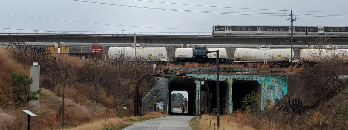 A MARTA train crosses a bridge above a walking trail