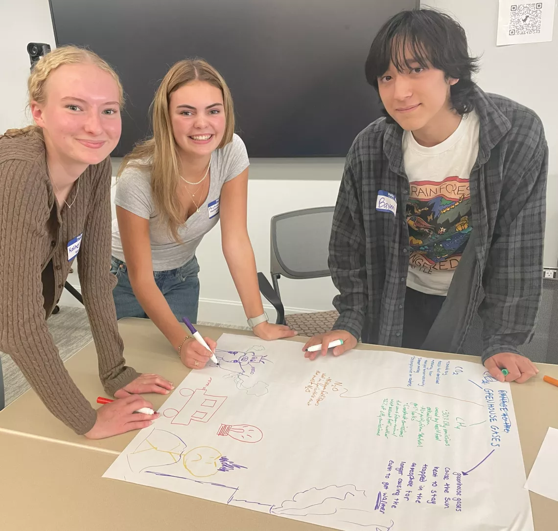 Three members of the Sierra Club youth group standing at a table making a poster.