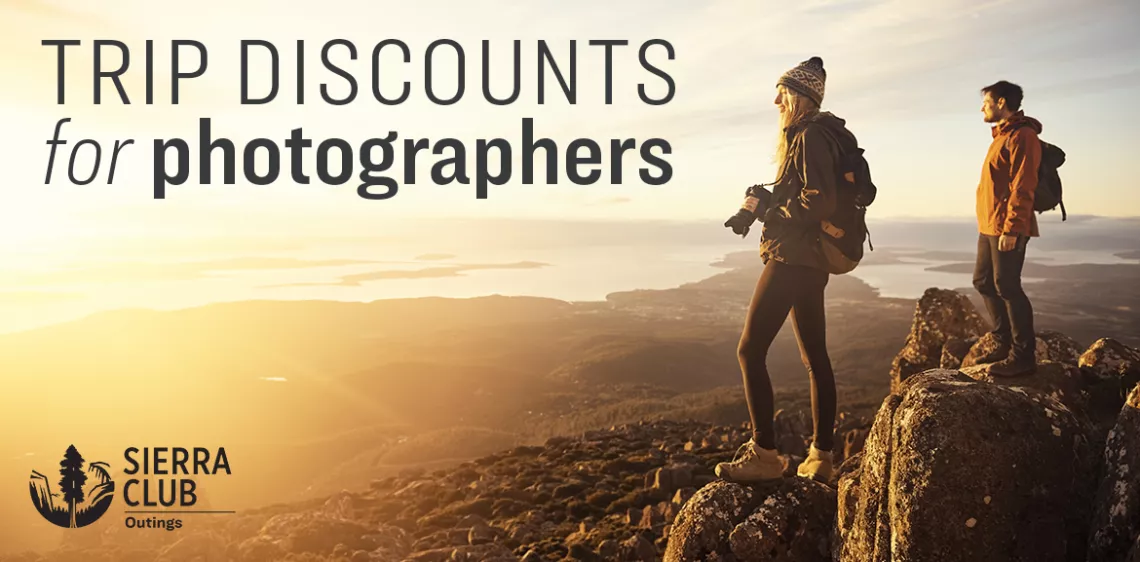 Two people stand on top of a mountain and one is holding a camera. Text overlaid on the image reads "Trip discounts for photographers."