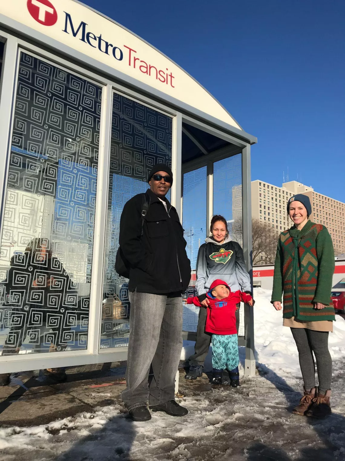 riders stand at a Metro Transit bus stop on a sunny winter day