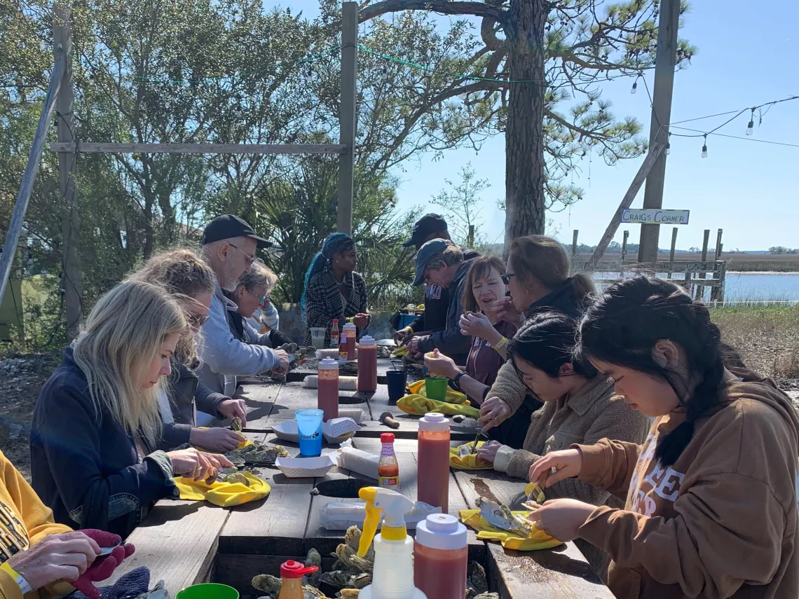 people standing around a table outdoors eating oysters