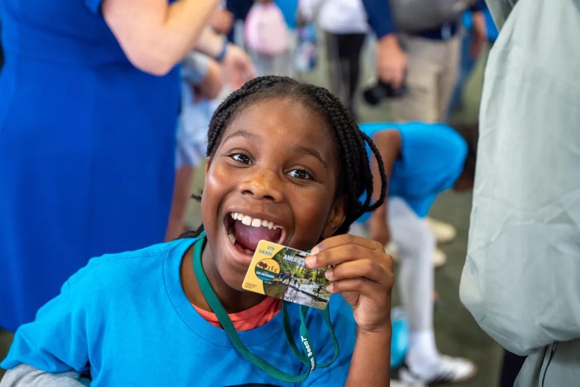 a girl with a large smile holds up her every kid outdoors pass