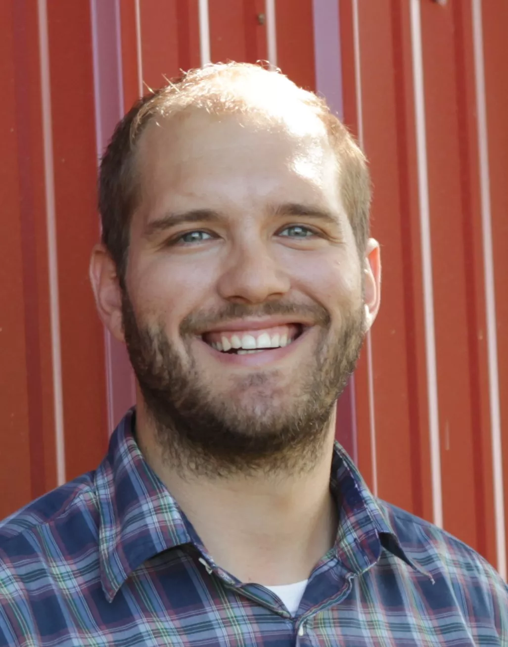 head shot of white guy in blue plaid shirt in front of red barn wall