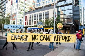 photo of demonstrators holding a banner: Energy We Can't Afford!