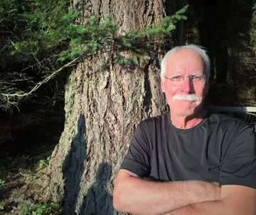 Man with white hair and moustache in front of redwood tree