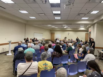 A room with a small crowd sitting in blue chairs.