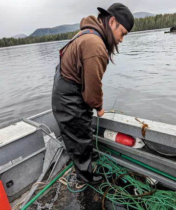 Lenard Stewart leans over a boat and pulls up a line from the water