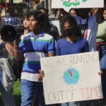 Picture of Nicholas & Nikita leading a march, holding a sign that says "We are running out of time" and a megaphone