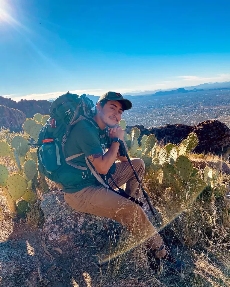 Miché Lozano sitting on a rock wearing a backpack atop a mountain