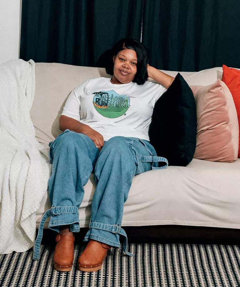 Kina Phillips wears a Stop the Burn shirt and jeans and sits on a sofa looking at the camera