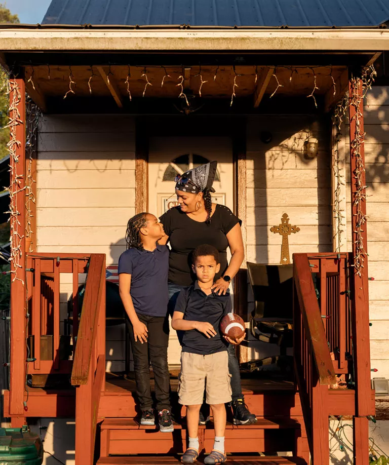 Luz Torres stands with her children on red wooden stairs in front of a house