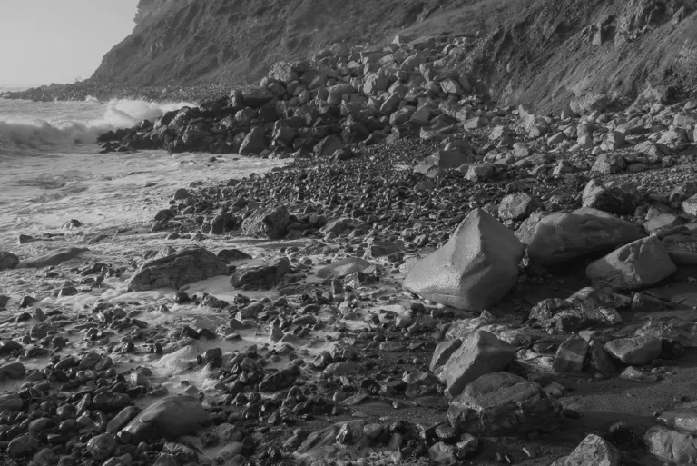 A rocky shore extends to the ocean from a cliff.