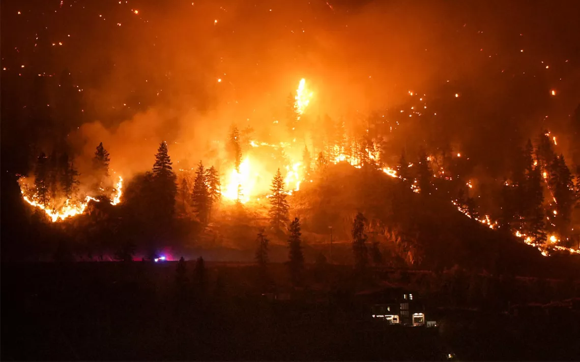 L'incendie de forêt de McDougall Creek brûle à flanc de montagne au-dessus d'une maison au bord du lac à West Kelowna, au Canada, le vendredi 18 août 2023