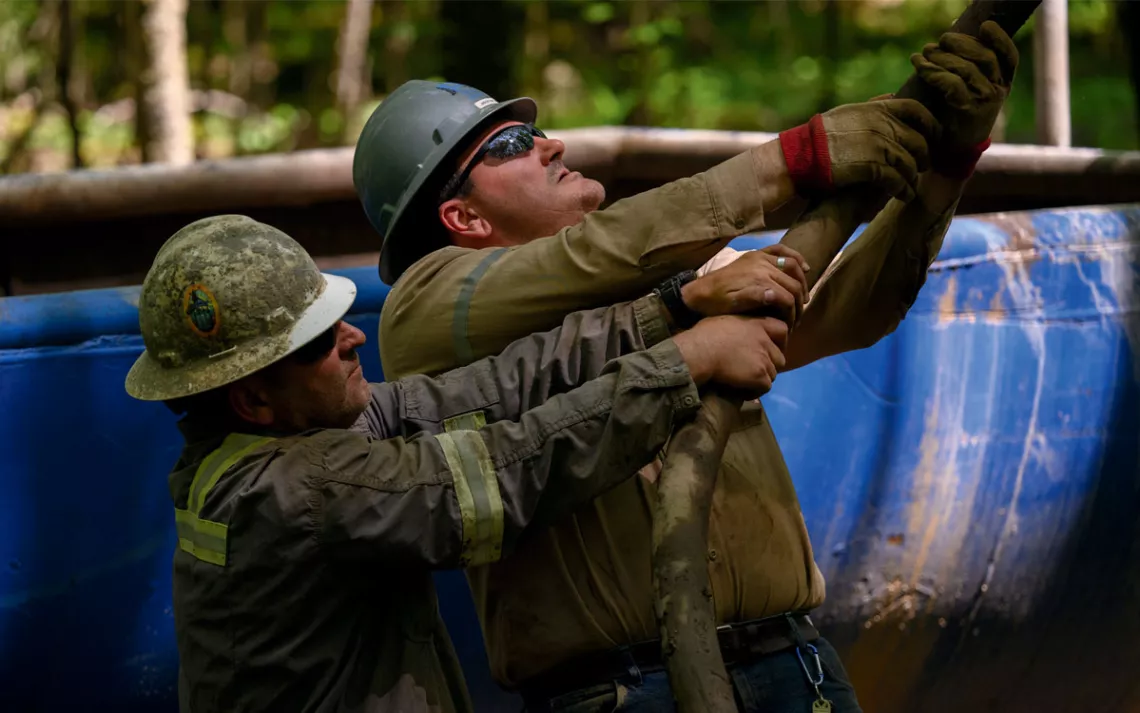 Two men in hardhats hold onto a cable at an abandoned oil well.