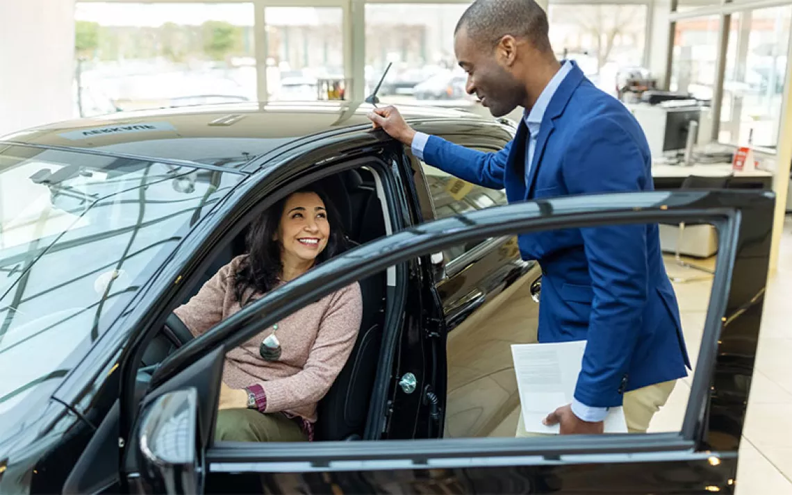 Car dealer explaining new car features to female customer at showroom.