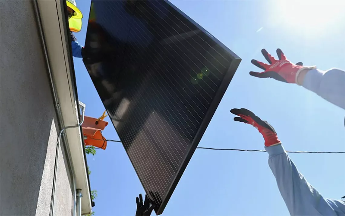 A worker hands off a solar panel being installed by another worker