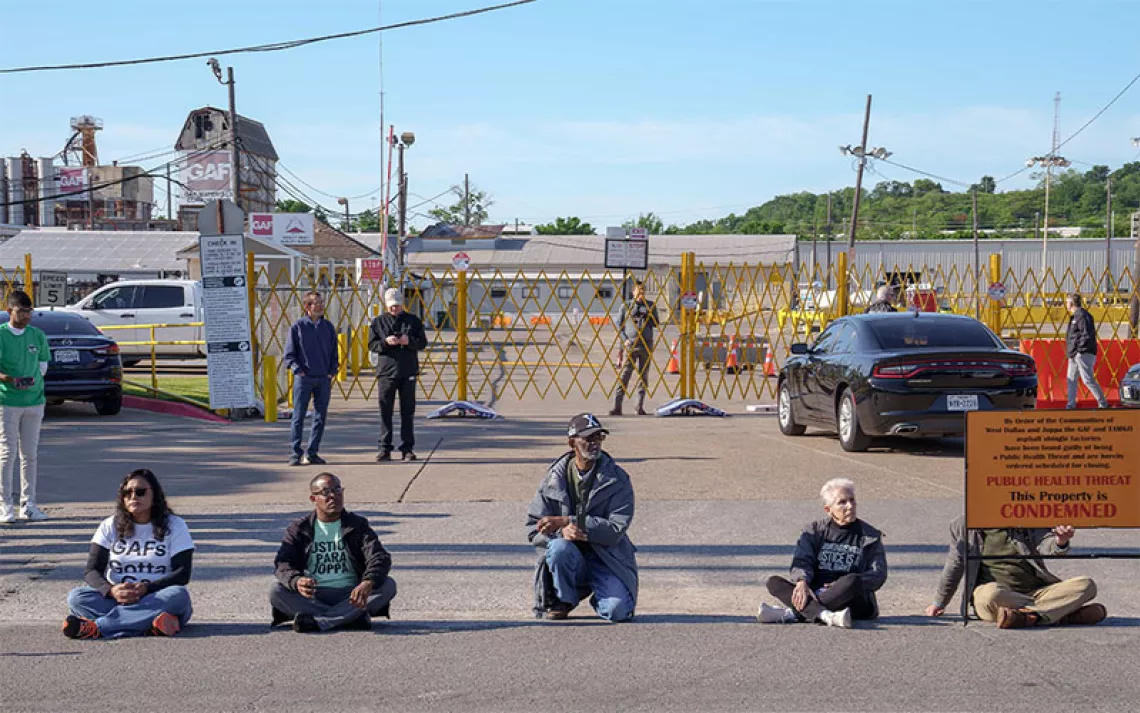 Janie Cisneros (left), who leads Singleton United/Unidos sits with four others in front of GAF on Earth Day 2024. The action was planned to raise awareness for a campaign aimed at closing the plant down. The shingles factory is one of the largest polluters in Dallas and has generationally affected the West Dallas neighborhood it operates in. | Photo by Johnathan Johnson 