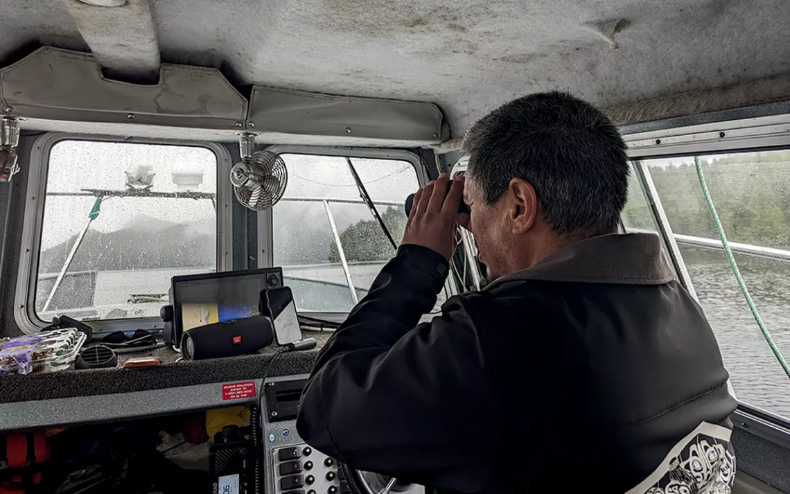 Howard Humchitt looks through binoculars out the window of a boat in the rain.