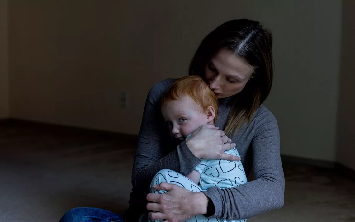 Amy Dishion hugs her toddler, who is looking over her shoulder at the camera