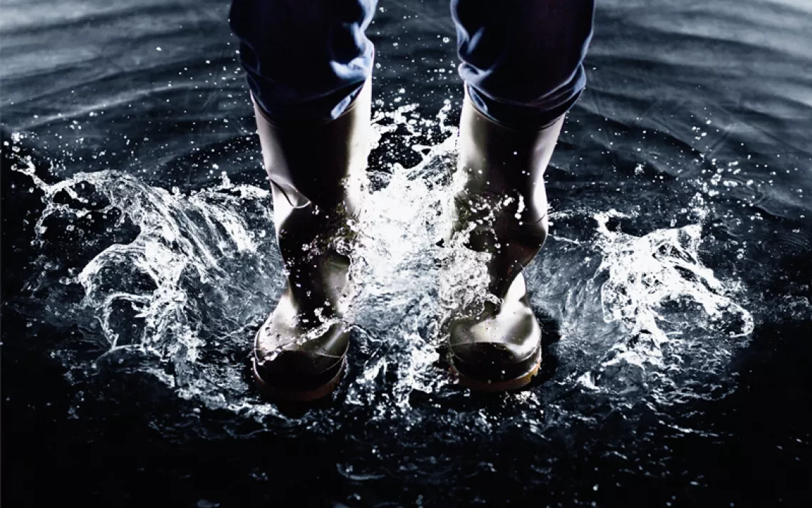 Close-up of someone's legs in rain boots as they splash in dark water