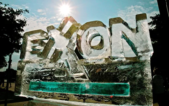 An ice sculpture in the shape of Exxon's logo slowly melting against a bright blue sky. 