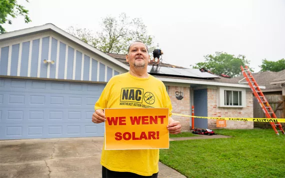 A man holds a "We Want Solar" sign outside his home.