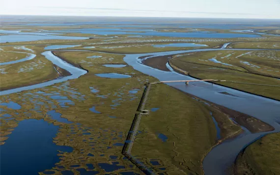 Aerial view of a sprawling muddy tundra and oil infrastructure in Alaska