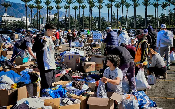 Two brothers look through donated clothes outside, palm trees behind them