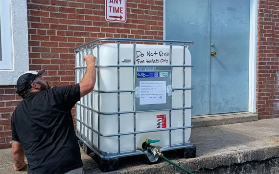 A large, plastic tank of water rests on a house's front porch